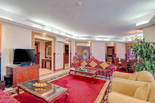 Wohnzimmer im Crowne Plaza Resort Salalah mit rotem Teppich, roten Sofas, Fernseher, Tisch und Pflanzen.