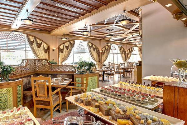 Innenansicht des Restaurants im Crowne Plaza Resort Salalah mit Holzmöbeln und einer Auswahl an Desserts.