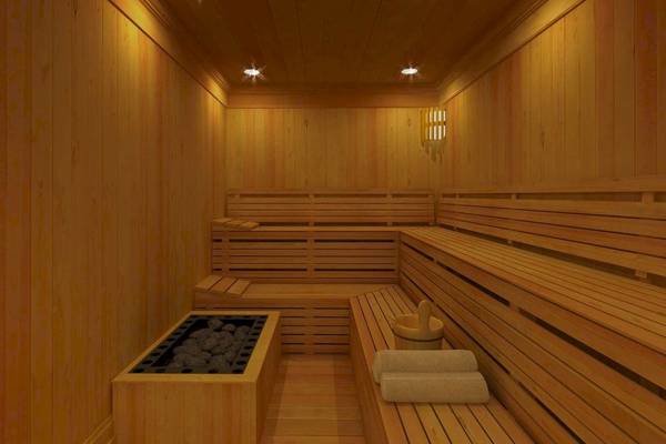Innenansicht einer Holzsauna im Alkyna Lifestyle Beach Resort mit Holzbänken, einem Feuerbecken und hellen Beleuchtungskörpern.