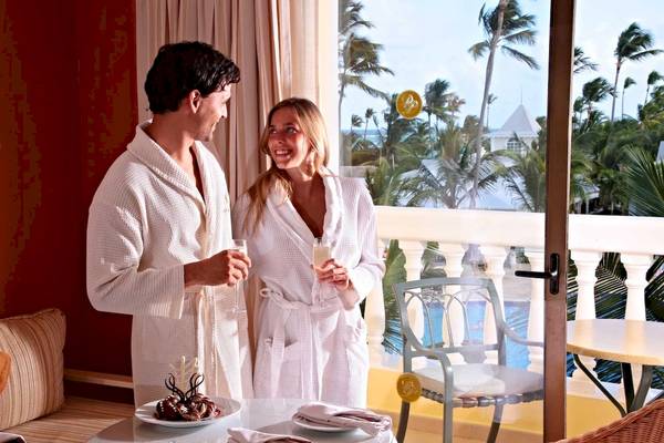 Mann und Frau auf Balkon im Bademantel mit Sektgläsern und Blick auf den Pool