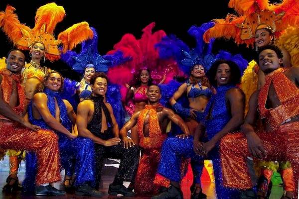 Gruppe von Performern in farbenfrohen Kostümen vor einer Bühne für eine Show im Bahia Principe Grand Bavaro Hotel.