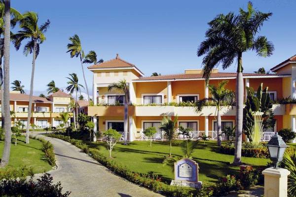 Außenansicht des Bahia Principe Grand Bavaro Hotels mit Gebäuden, Palmen und gepflegtem Rasen.