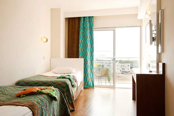 Ein modernes Schlafzimmer im Seaden Sea World Resort & Spa mit zwei Betten, blauen Vorhängen und einem großen Glasfenster, das auf einen Balkon hinausgeht.
