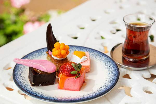Eine Platte mit verschiedenen Desserts und ein Glas Tee auf einem Tisch.