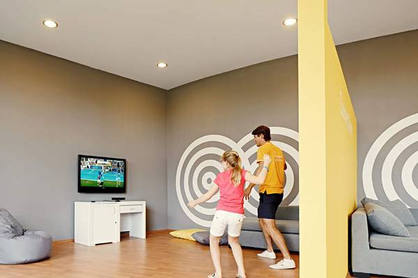 Ein Kinderzimmer mit Fernseher, Sofa und Zielwand, in dem zwei Kinder spielen.
