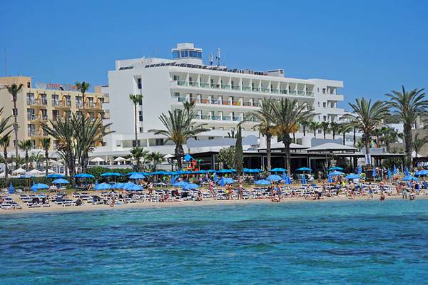Strand vor dem Nelia Beach Hotel & Spa mit vielen Gästen und blauen Sonnenschirmen