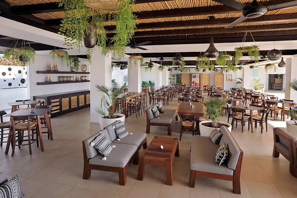 Innenbereich des Restaurants des Nelia Beach Hotel & Spa mit Holztischen, Stühlen und Pflanzen.