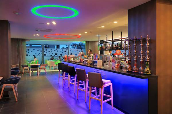 Barbereich im Nelia Beach Hotel & Spa mit blauen und grünen Beleuchtungselementen und Hockern an der Theke.