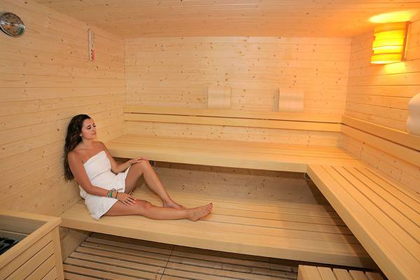 Eine Frau in einem weißen Handtuch sitzt in einer Holzsauna im Nelia Beach Hotel & Spa.