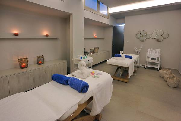 Spa-Massageraum im Nelia Beach Hotel & Spa mit zwei Massagetischen, blauen Handtüchern und dekorativen Elementen.