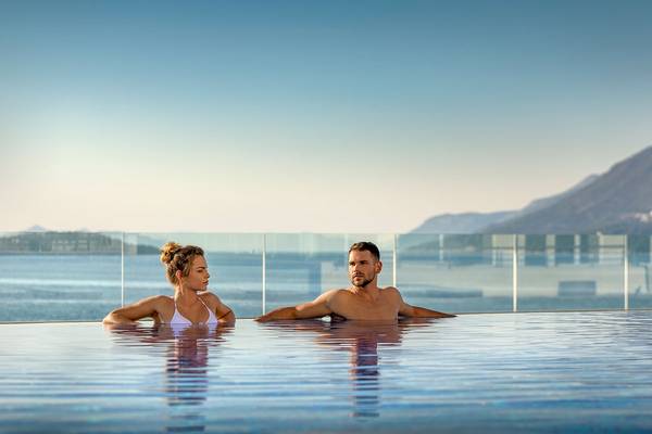 Paar im Pool vor dem Hotel Valamar Argosy mit Blick auf das Meer und die Berge.
