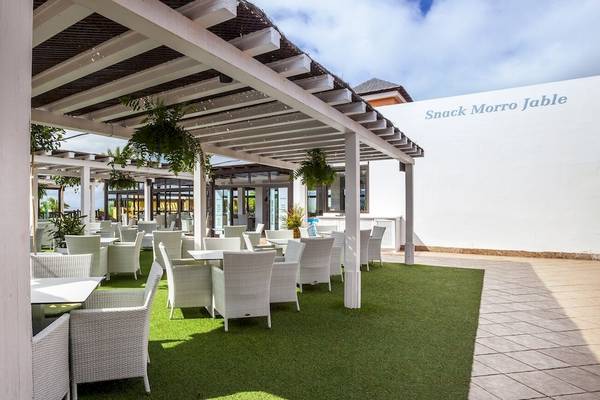 Terrasse des Occidental Jandia Playa Hotels mit Tischen und Stühlen unter einer Laube.