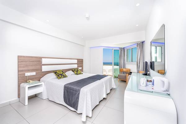 Ein modernes Zimmer im Tasia Maris Sands Hotel mit einem Bett, Nachttischen und einem Schreibtisch.
