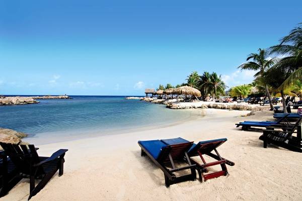 Strand des LionsDive Beach Resorts mit weißen Sand, blauem Wasser und Liegen.