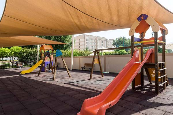 Kinderspielplatz unter einem Sonnensegel mit Rutschen und Schaukeln im Freien.