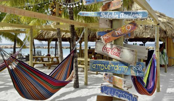 Strand des LionsDive Beach Resort mit bunten Himmelbetten und blauem Himmel