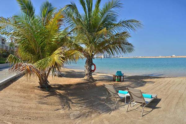 Strandansicht von Jannah Hotels Resorts & Villas mit zwei Sonnenliegen und Palmen.