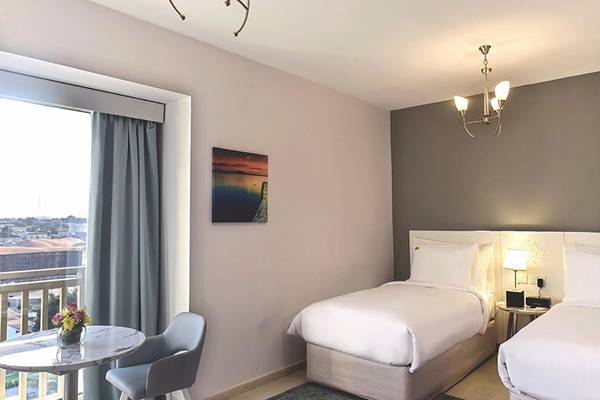 Innenansicht eines Hotelzimmers von Jannah Hotels Resorts & Villas mit zwei Betten, einem Tisch und einem Balkon.