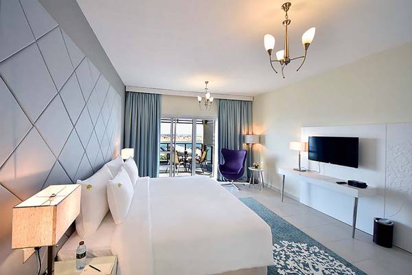 Innenansicht eines Schlafzimmers im Jannah Hotels Resorts & Villas mit großem Bett, Fernseher, Tisch und Balkon