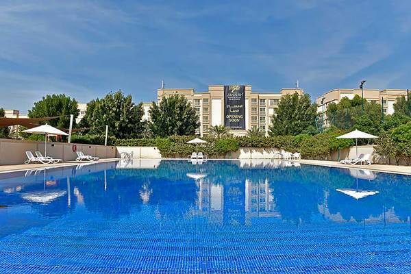 Ein Swimmingpool mit weißen Sonnenliegen und Sonnenschirmen vor dem Jannah Hotels Resorts & Villas Gebäude.