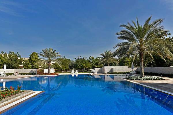 Ein blauer Swimmingpool im Freien des Jannah Hotels Resorts & Villas mit Palmen und Sonnenliegen.
