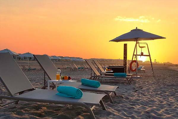 Strand mit Lounge-Sesseln und einem Sonnenuntergang im Hintergrund bei Jannah Hotels.