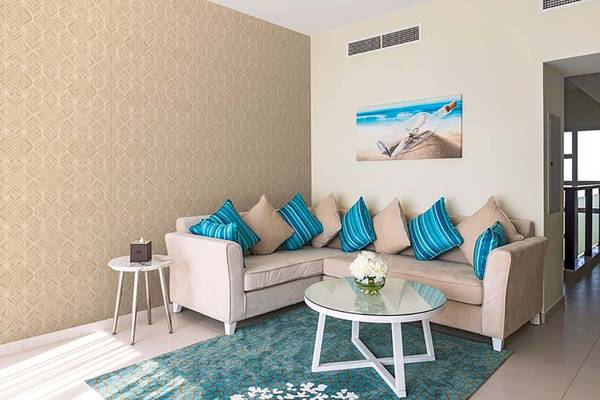 Wohnzimmer mit beigem Sofa, blauen Kissen, Tisch mit Blumenvase und dekorativem Bild an der Wand.