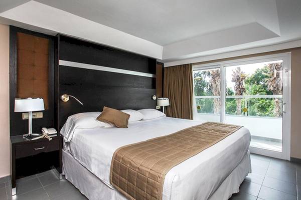Ein Hotelzimmer im Riu Naiboa mit einem Bett und einem Balkon mit Ausblick auf Palmen.