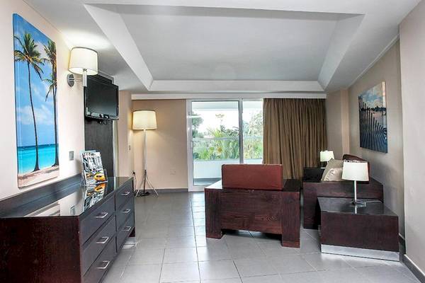 Wohnbereich im Riu Naiboa Hotel mit Sofa, Fernseher und Kunstwerken an der Wand.