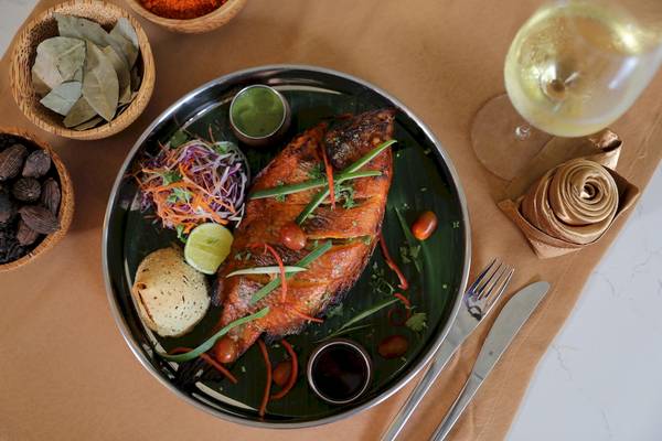 Gegrillter Fisch auf einem Teller, umgeben von Gemüse, Gewürzen und einem Glas Wein.