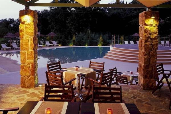 Außenbereich des Ariti Grand Hotel Corfu mit beleuchteten Tischen und Stühlen am Pool.