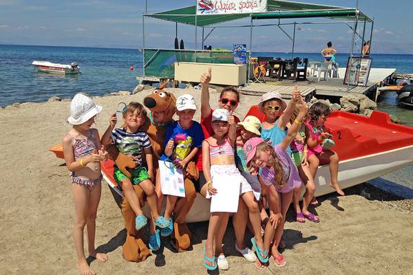 Kinder mit Maskottchen auf dem Strand neben einem Wassersport-Boot