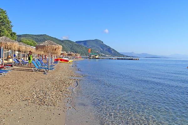 Strand des Messonghi Beach Holiday Resort mit Sonnenliegen, Sonnenschirmen und Booten im Wasser