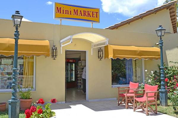 Außenansicht des Mini Markets vor dem Messonghi Beach Holiday Resort mit gelben Vordächern und roten Stühlen.