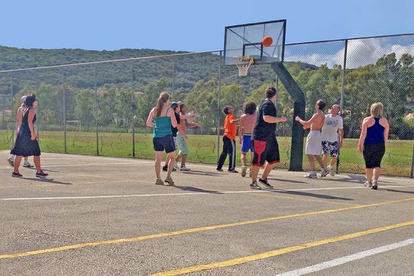 Mehrere Personen spielen Basketball auf einem Freiplatz, mit einem Bergpanorama im Hintergrund.