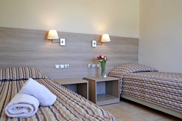 Zwei Betten im Hotelzimmer von Messonghi Beach Holiday Resort mit gestreiften Laken und Kissen, Nachttischen und Nachtlampen an der Wand.