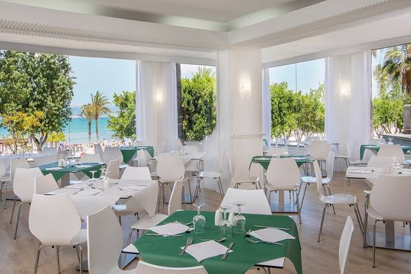 Restaurantbereich des Whala Beach Hotel mit Blick auf das Meer und eine bevölkerte Strandpromenade.