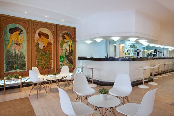 Loungebereich des Whala Beach Hotel mit weißen Stühlen und Tischen, einer Theke und Wandmalereien.