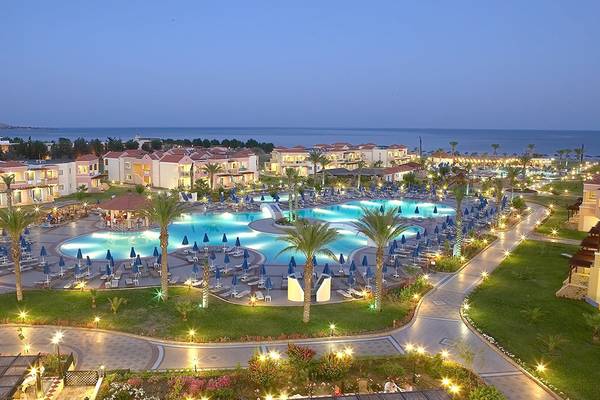 Abendansicht des Lindos Princess Beach Hotels mit Pool, Sonnenliegen und Palmen.