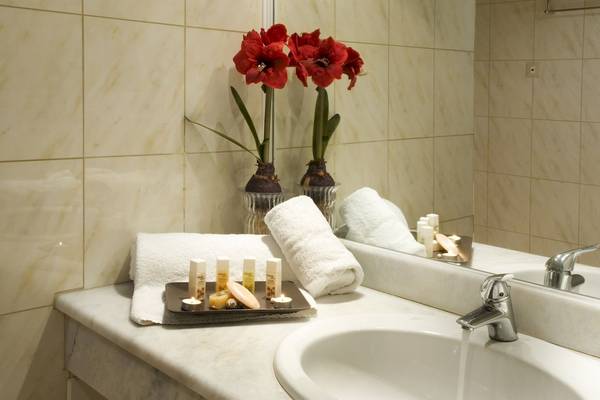 Badezimmer im Ariti Grand Hotel Corfu mit roten Amaryllis, Handtüchern und Waschartikeln.