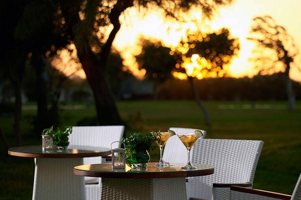 Sitzplätze im Freien am Mitsis Ramira Beach Hotel bei Sonnenuntergang mit Getränken auf dem Tisch.