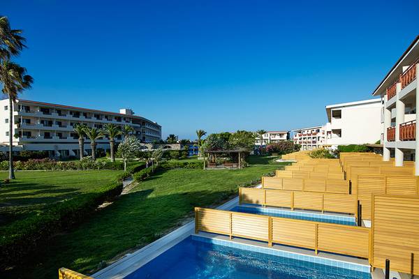 Außenpool neben dem Mitsis Ramira Beach Hotel, umgeben von Rasen und Gebäuden.