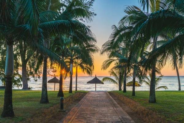 Sonnenuntergang am Strand des Le Meridien Ile Maurice Hotels mit Palmen und Sonnenschirmen.