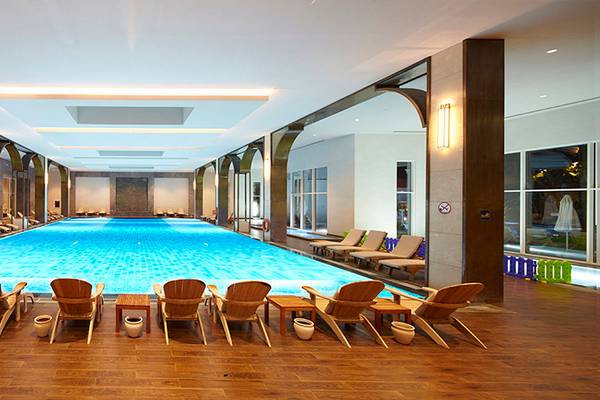 Innenpool des Titanic Deluxe Golf Belek Hotels mit runden Holzstühlen und Tischen.