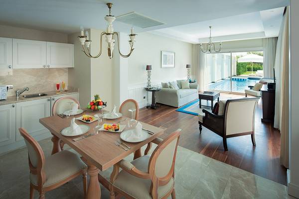 Suite-Esszimmer im Titanic Deluxe Golf Belek mit Esstisch, Früchteteller und Swimmingpool im Hintergrund.