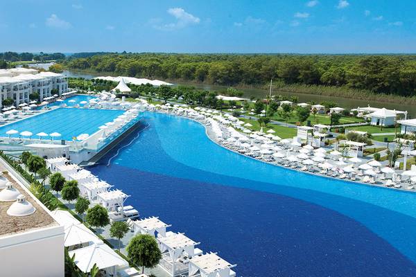 Luftaufnahme des Titanic Deluxe Golf Belek Resorts mit riesigem Infinity-Pool und weißen Sonnenschirmen.