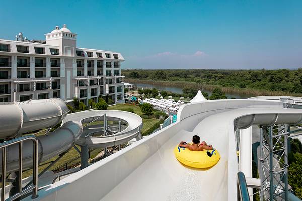 Ein Mann rutscht auf einer gelben Schwimmringrutsche auf einer Wasserrutsche im Titanic Deluxe Golf Belek Hotel.