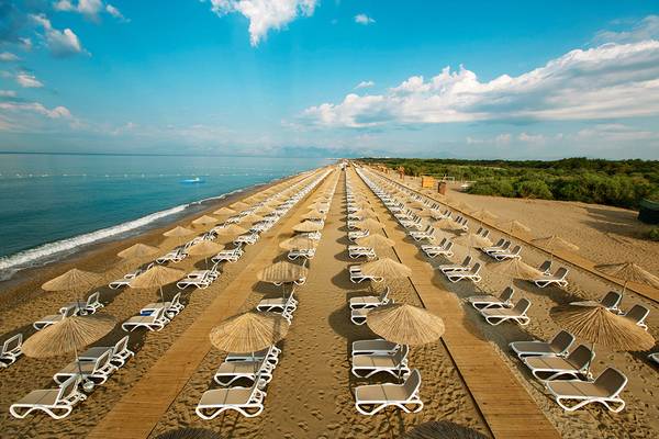 Luftaufnahme des Titanic Deluxe Golf Belek Strandes mit vielen Sonnenliegen und Strohschirmen.