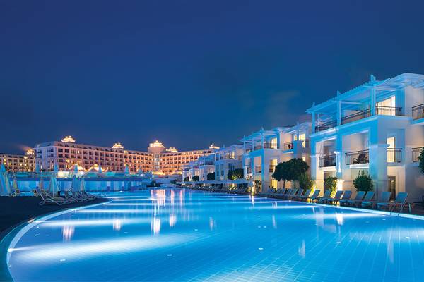 Poolbereich des Titanic Deluxe Golf Belek Hotels bei Nacht mit illuminierten Gebäuden und Loungestühlen