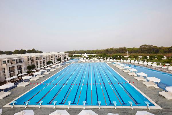 Olympisches Schwimmbecken im Hotel Titanic Deluxe Golf Belek mit vielen weißen Sonnenschirmen und Liegestühlen.